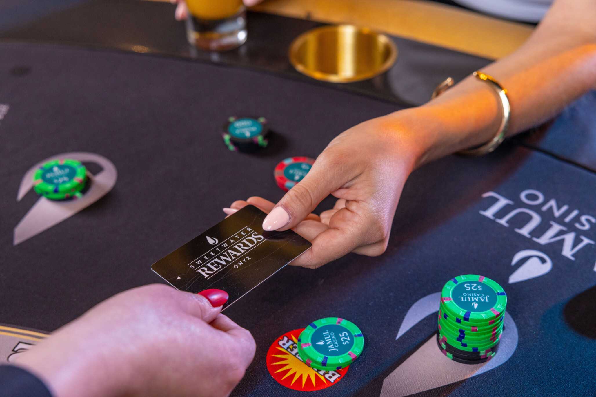A woman hands over her Sweetwater Rewards Card over a blackjack table.